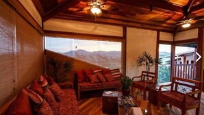 A cozy room with a wooden ceiling, a sofa set, a coffee table, and a view of mountains through large windows. - Estrada Real Palace Hotel (Brumadinho)