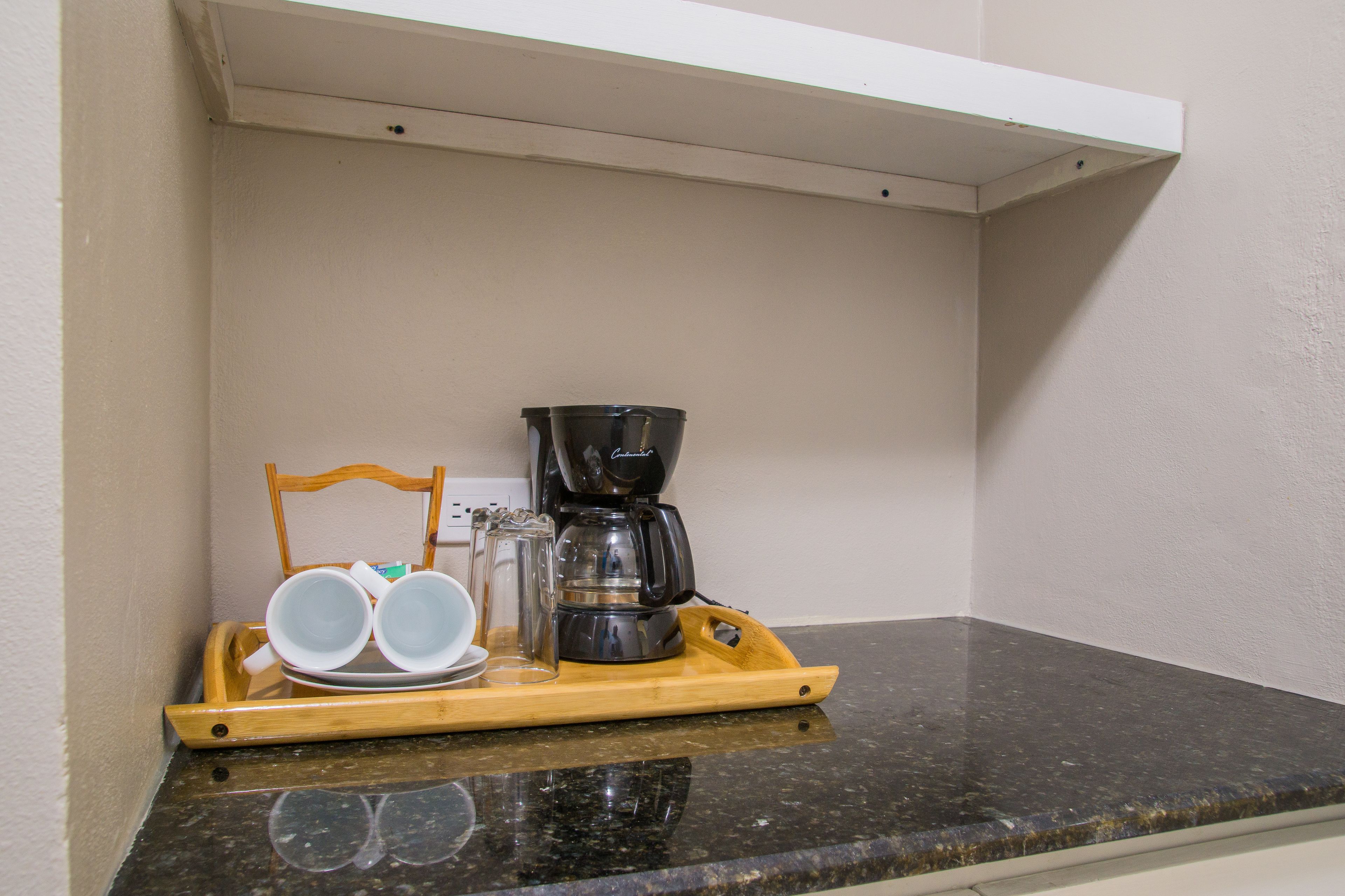 A kitchen counter with a coffee maker, a tray with cups and a glass, and a wooden chair.