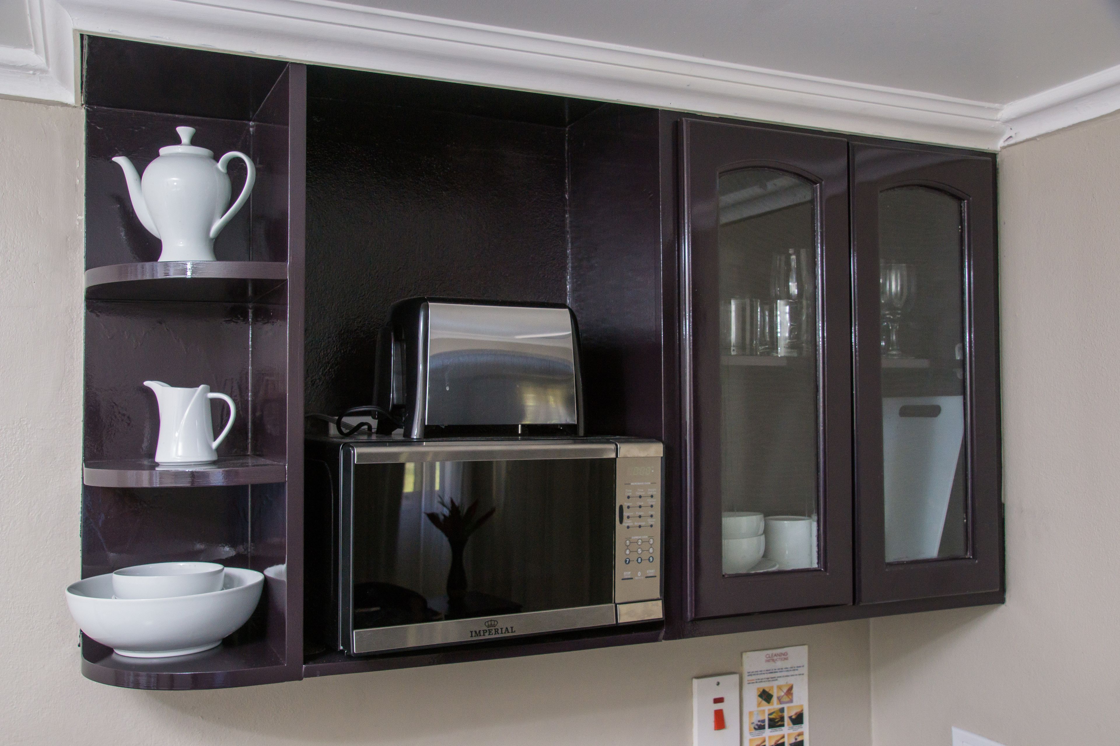 A kitchen with a microwave, toaster, and shelves holding white dishes.