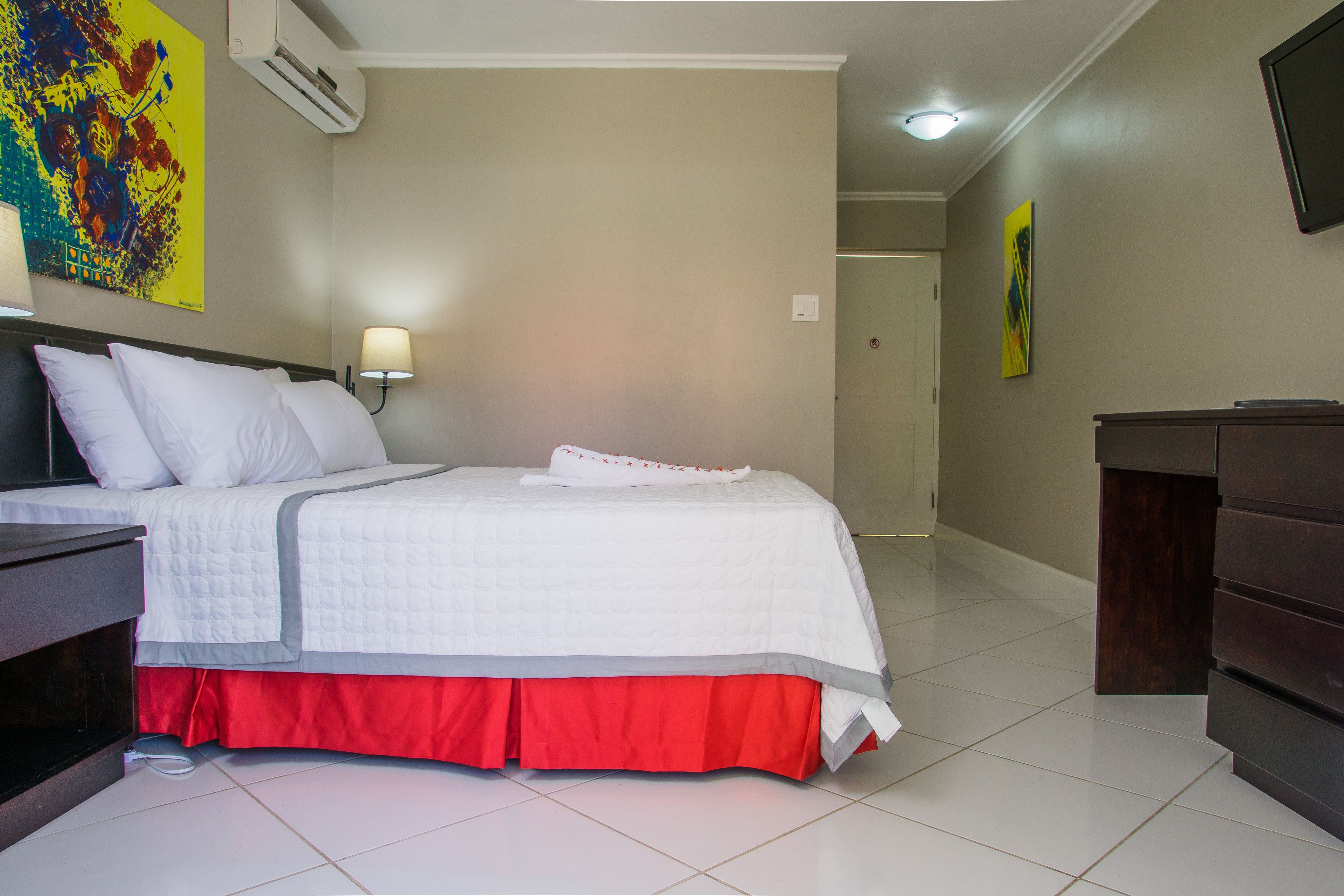 A hotel room with a bed, a desk, a lamp, and a dresser.