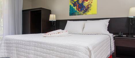 A hotel room with a large bed, a wardrobe, two bedside lamps, and a colorful abstract painting on the wall.