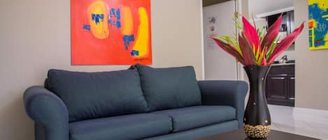 A living room with a blue sofa, a black vase with red and yellow flowers, and a colorful abstract painting on the wall.