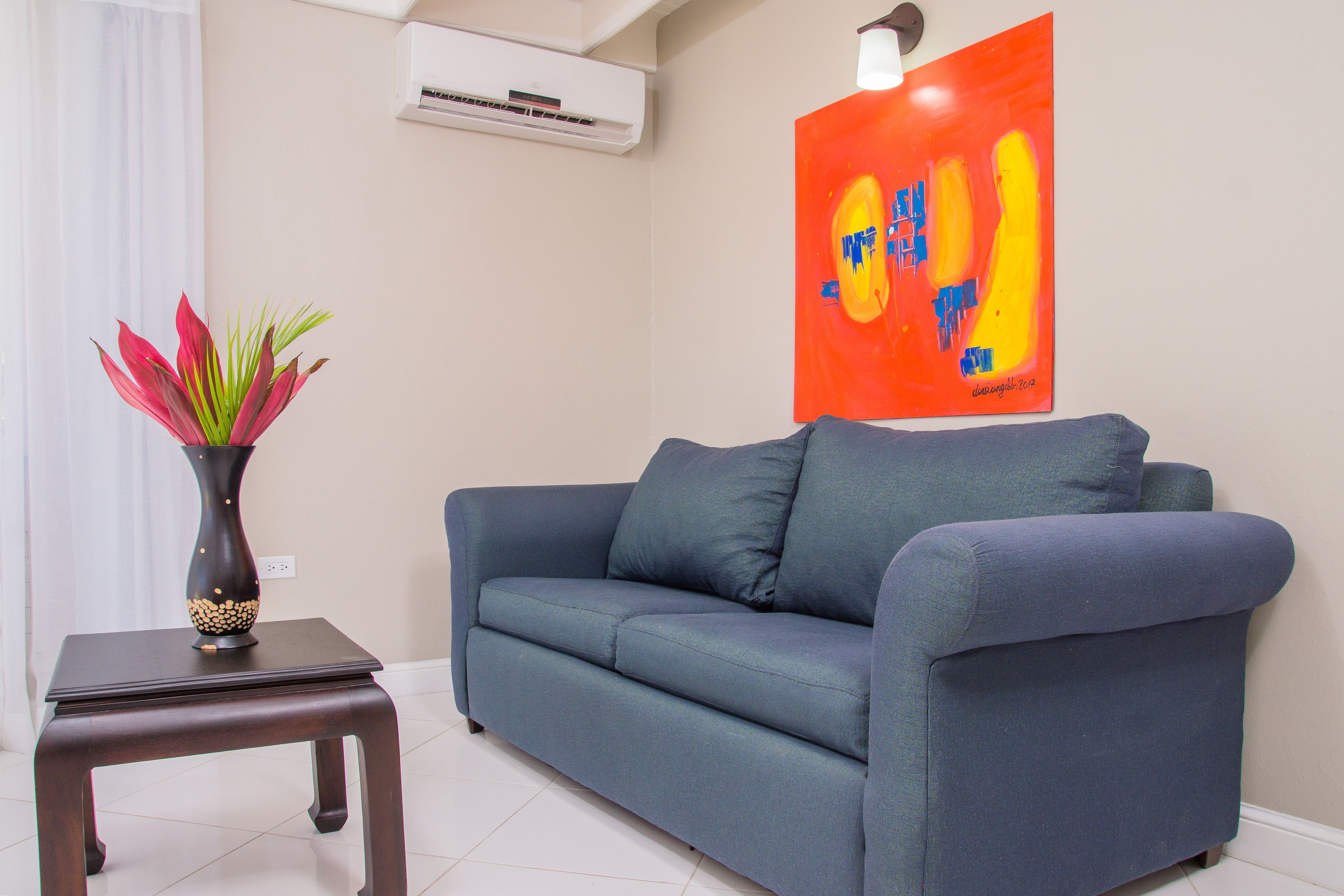 A blue sofa, a small table with a vase, and a wall with a colorful artwork.