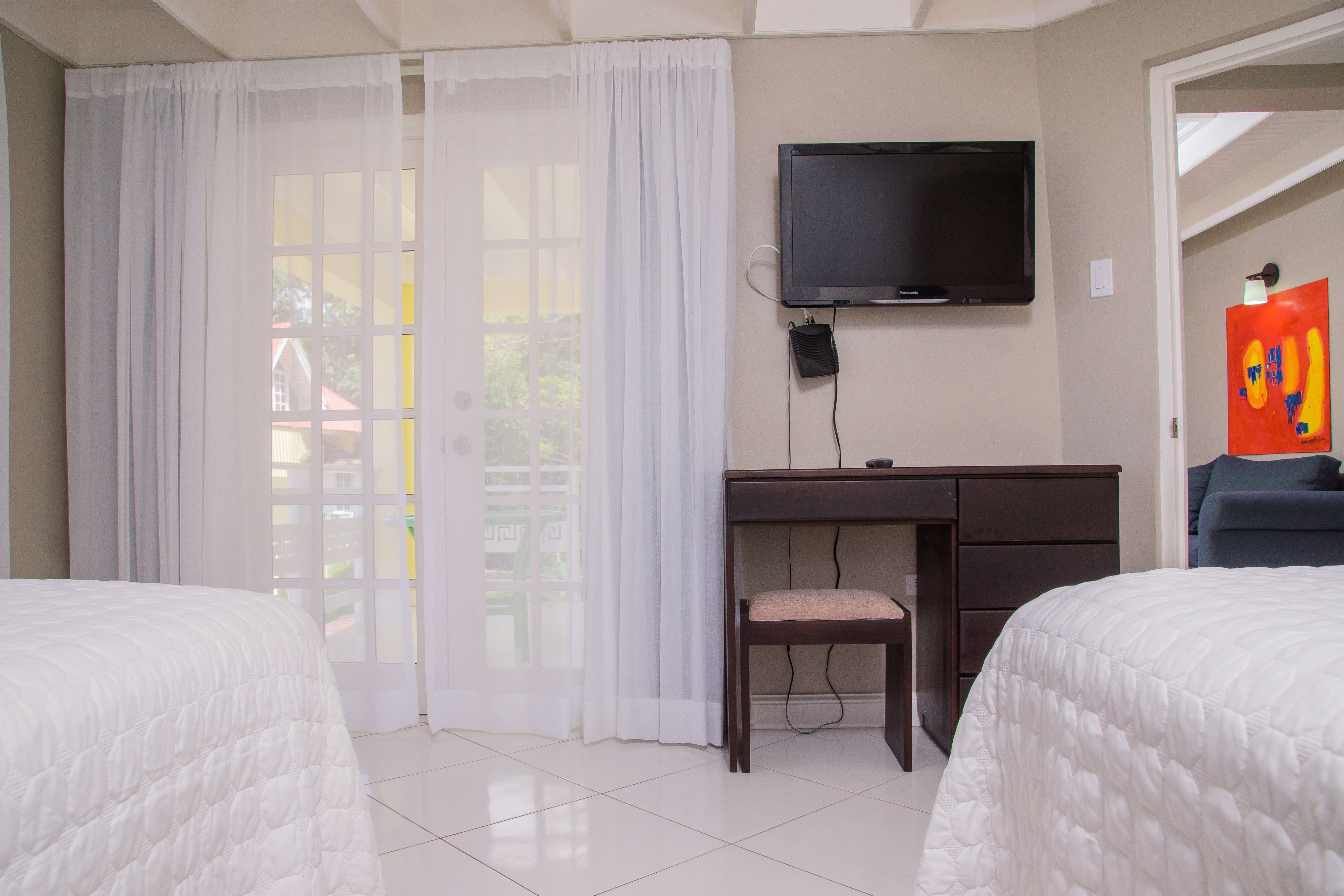 A hotel room with two beds, a desk, a chair, a TV, and a painting on the wall.