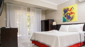 A hotel room with a bed, a desk, a lamp, and a colorful abstract painting on the wall.