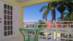 A balcony with a green table and chairs, white walls, and a view of palm trees and buildings.