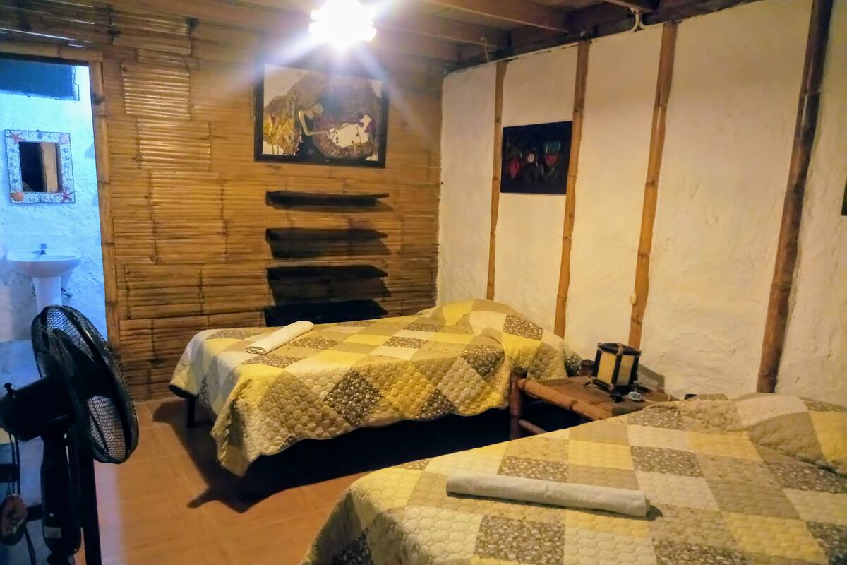 Une chambre confortable avec deux lits, un ventilateur, un lavabo et un tableau accroché au mur.
