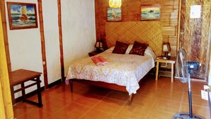 A wooden room with a bed, two paintings, a table, and a fan. - Guacamayo Bed & Breakfast (Máncora)