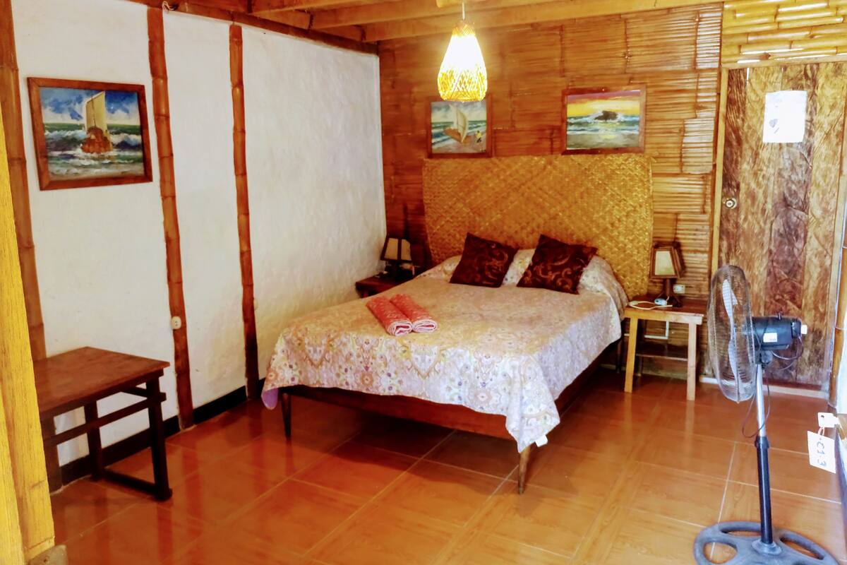 Une pièce en bois avec un lit, deux tableaux, une table et un ventilateur.