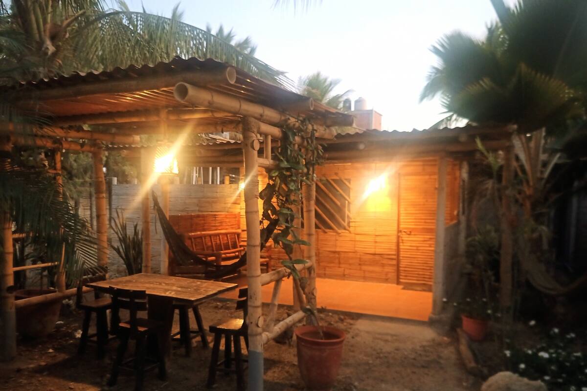 Un espace extérieur aménagé dans un style rustique, avec une table et des chaises en bois, un hamac et une structure en bois servant d’abri contre le soleil.