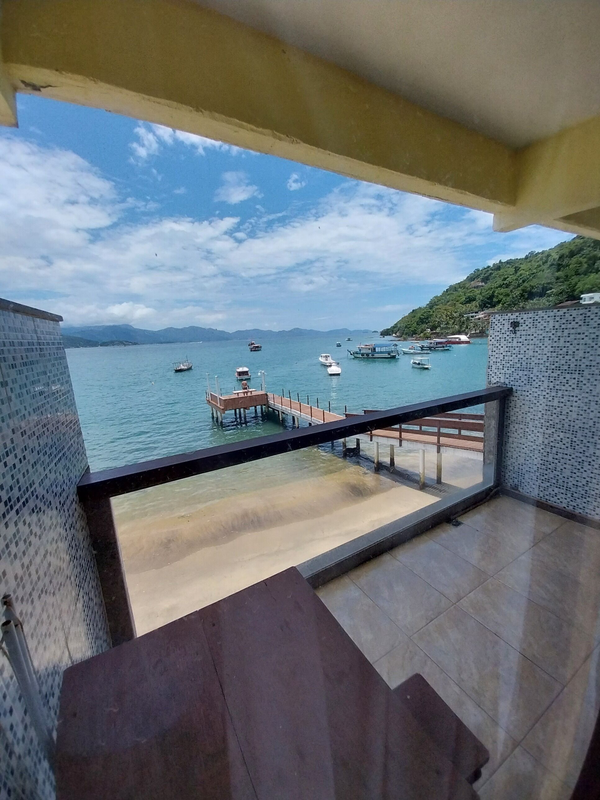A balcony with a view of a calm sea, boats, and a pier.