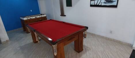 A room with a pool table, a foosball table, and a painting on the wall.