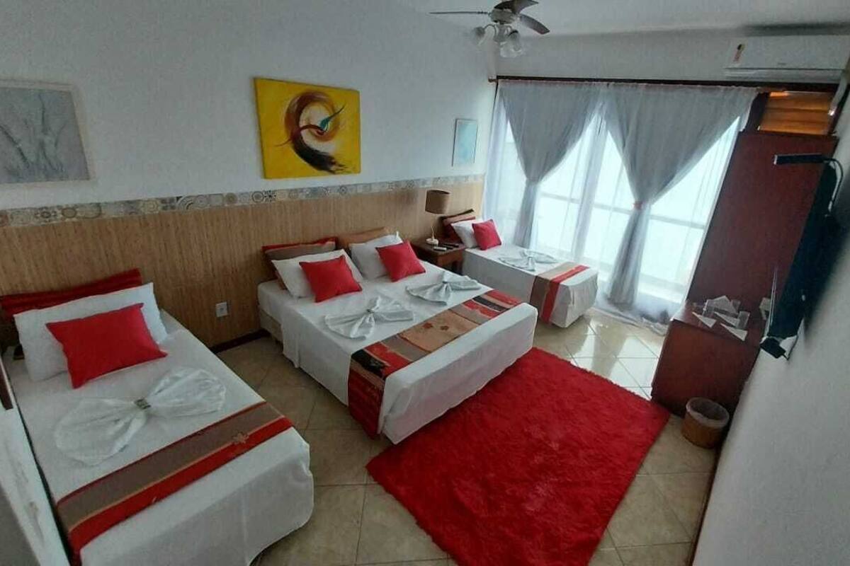 A hotel room with two beds, a red rug, a ceiling fan, and a window with curtains.