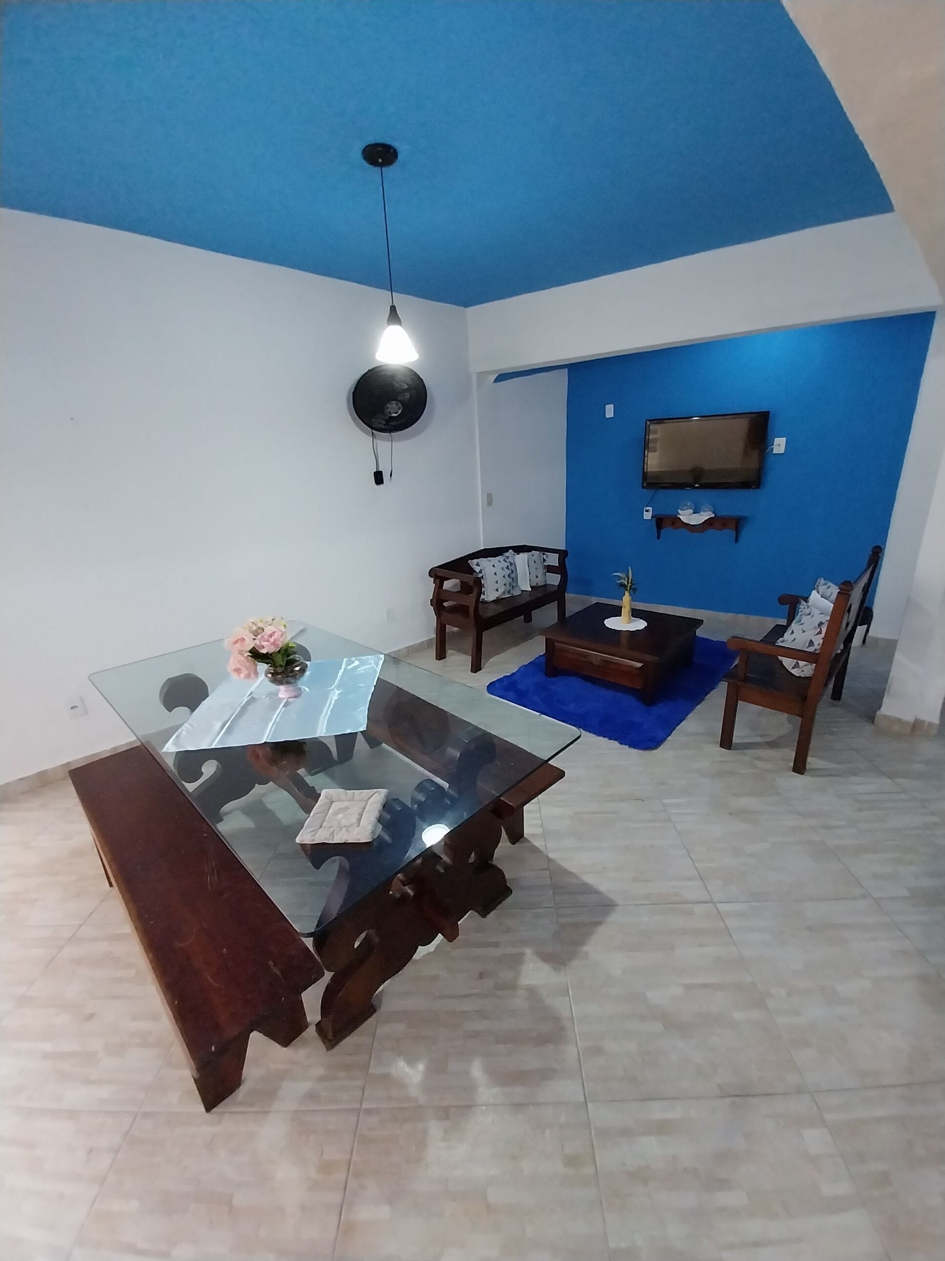 A modern living room with a glass-top dining table, a sofa, and a TV mounted on the wall.