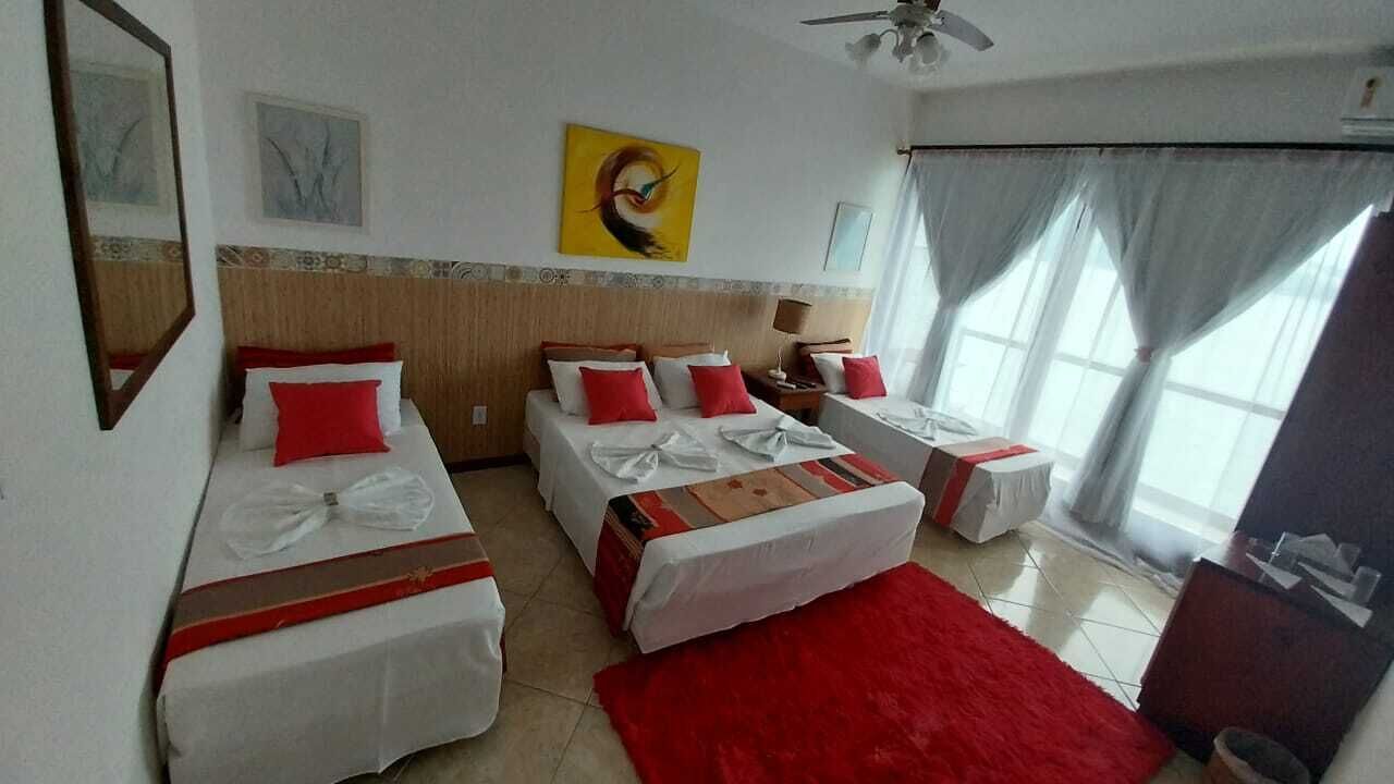 Une chambre d’hôtel avec trois lits, un tapis rouge et un ventilateur de plafond.