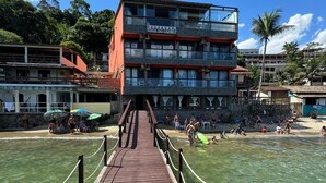 A wooden boardwalk leading to a building with multiple balconies, surrounded by a beach and palm trees. - Pousada Toca do Cambú (Angra dos Reis)