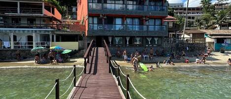 Un muelle de madera que conduce a un edificio con varios balcones con vista a una playa.