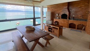 A spacious kitchen with a brick oven and a large window overlooking a body of water. - Pousada Toca do Cambú (Angra dos Reis)