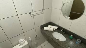 A bathroom with white tiled walls, a white toilet, a sink with a granite countertop, and a mirror.