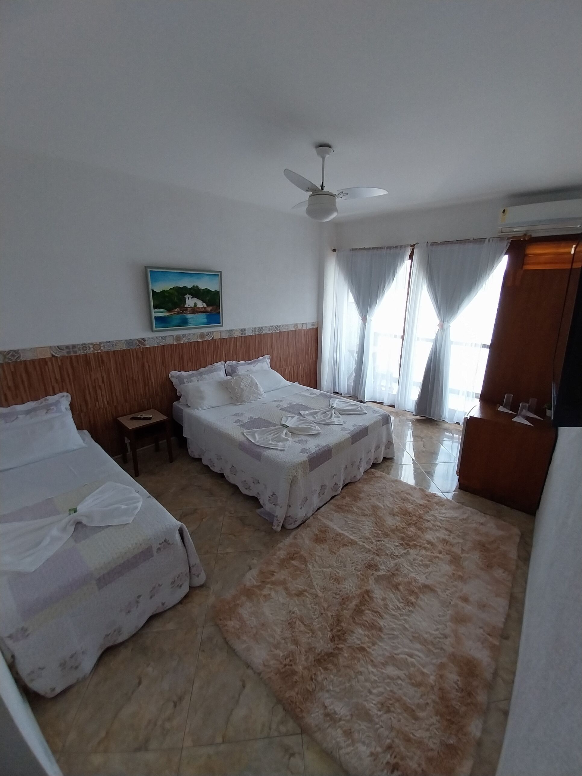 A hotel room with two beds, a ceiling fan, a painting on the wall, and a large rug.