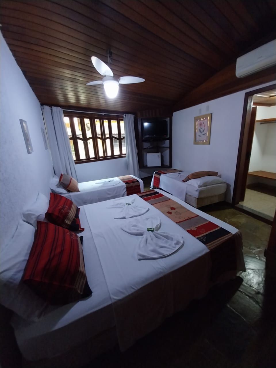 A room with two single beds, a ceiling fan, a television, and a window with curtains.