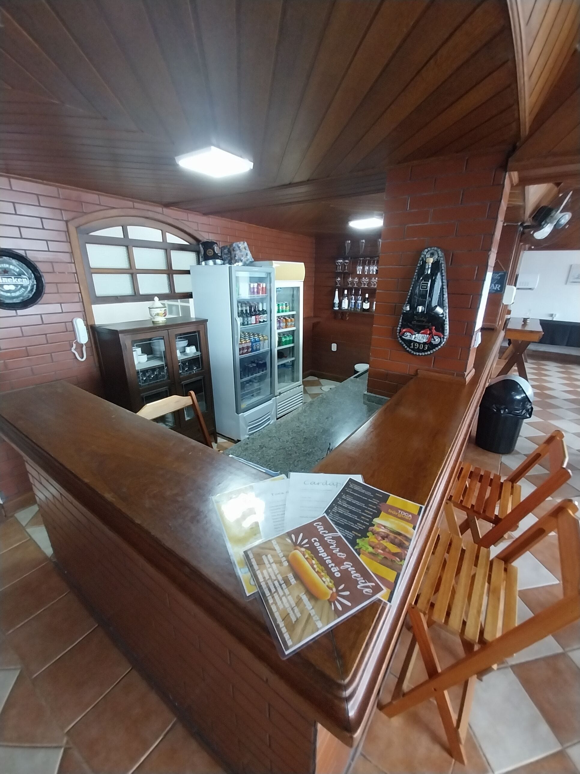 A bar area with a counter, wooden chairs, a refrigerator stocked with beverages, and a wall-mounted menu.