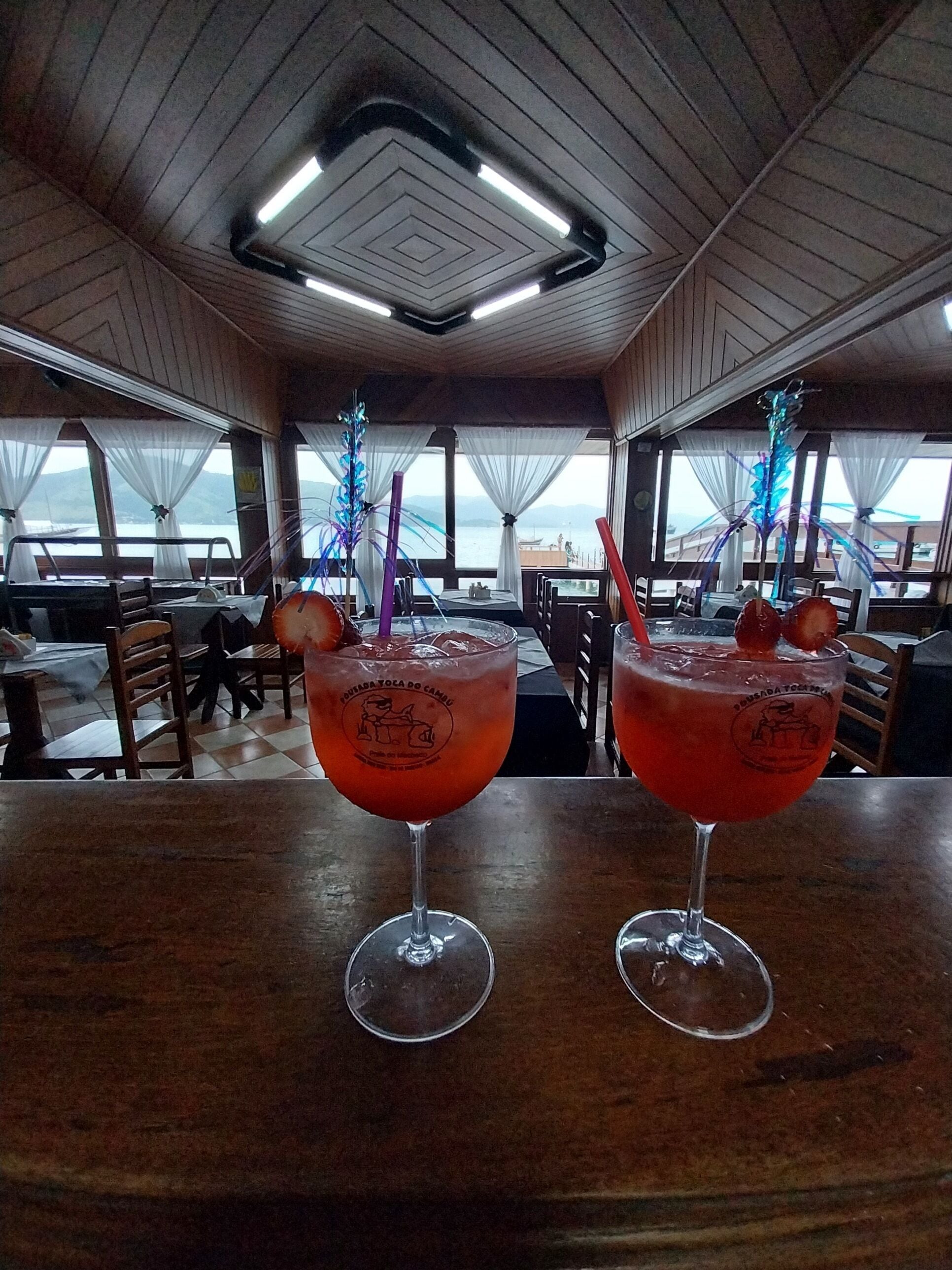 Two cocktails on a wooden table in a restaurant with a view of the sea.