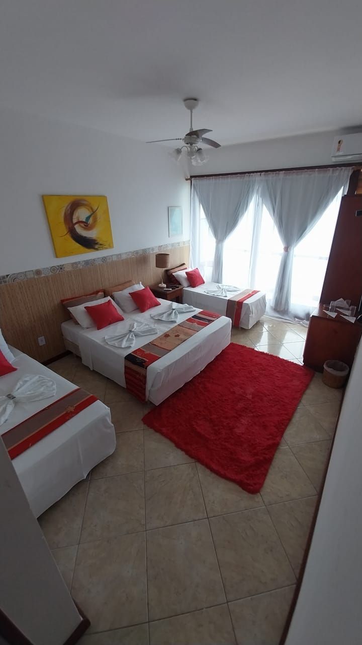 Een hotelkamer met twee bedden, een rood tapijt, een plafondventilator en een schilderij aan de muur.
