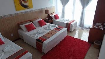 Een hotelkamer met twee bedden, een rood tapijt, een plafondventilator en een schilderij aan de muur.