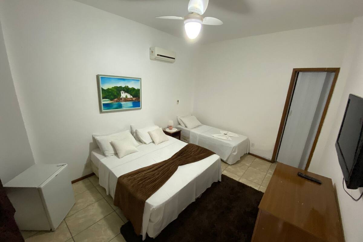A hotel room with a bed, a smaller bed, a desk, a chair, a TV, and a painting on the wall.