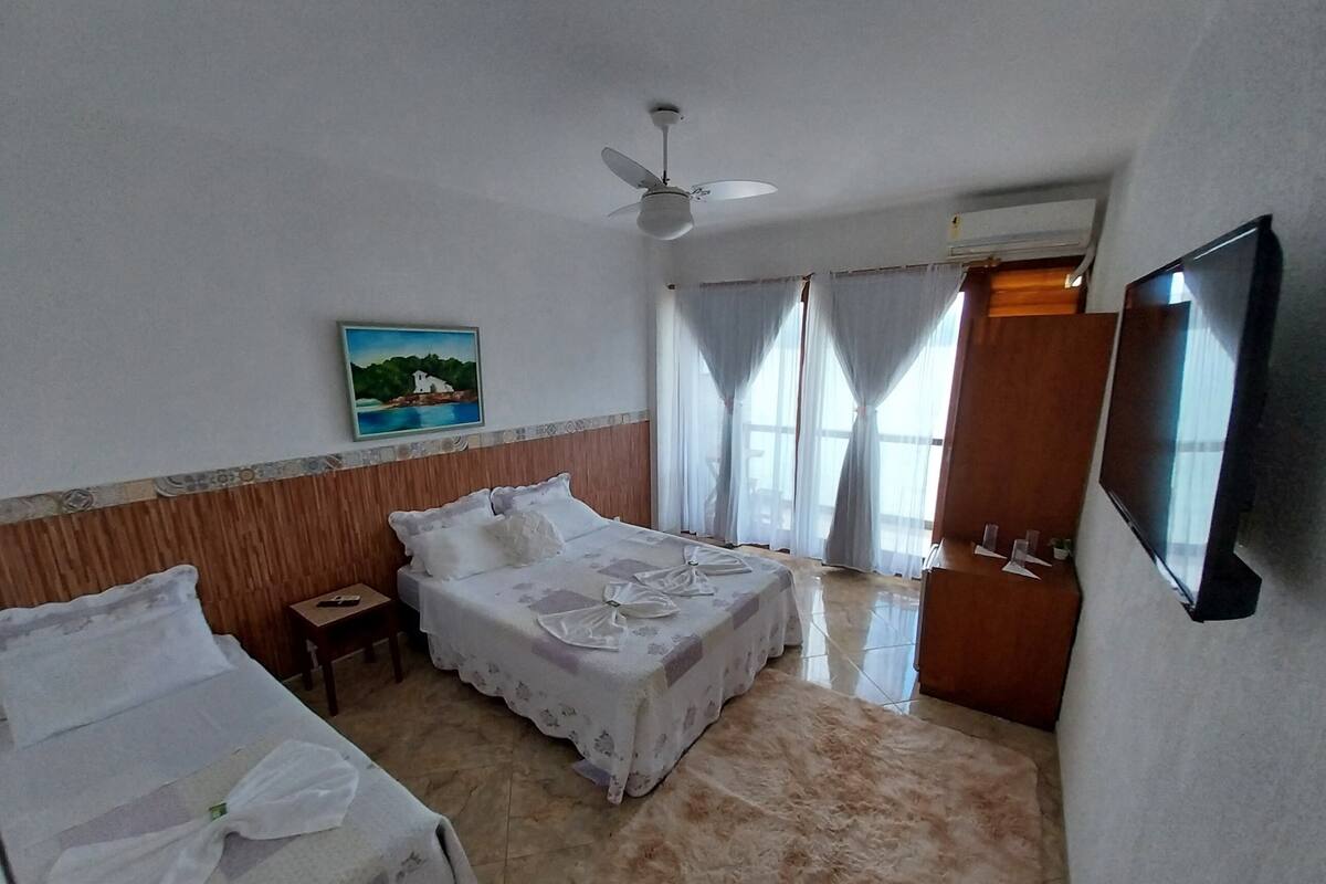 A hotel room with two beds, a ceiling fan, a painting, and a TV on the wall.