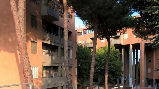 A courtyard with brick pathways, trees, and multi-story buildings with balconies. - Vacanza a Casa (Rome)
