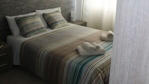 A neatly made bed with striped bedding, a headboard, and a nightstand with a lamp. - Vacanza a Casa (Rome)