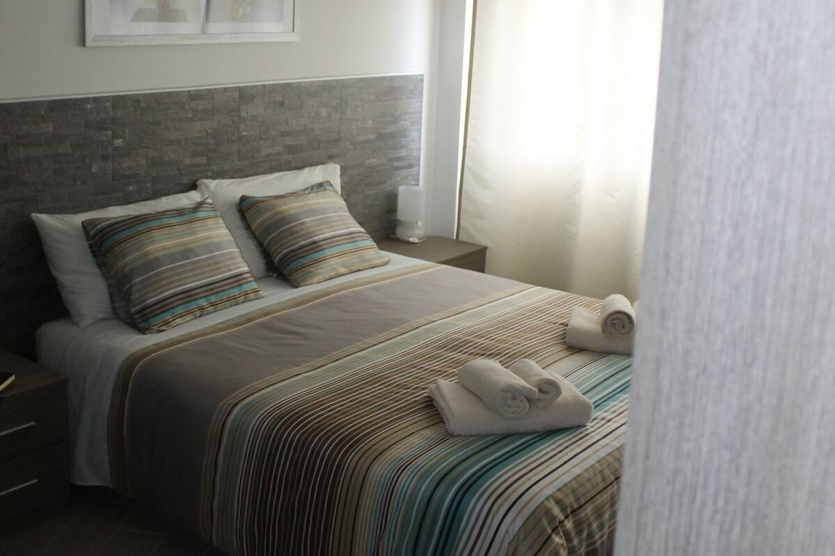 A neatly made bed with striped bedding, a headboard, and a nightstand with a lamp.