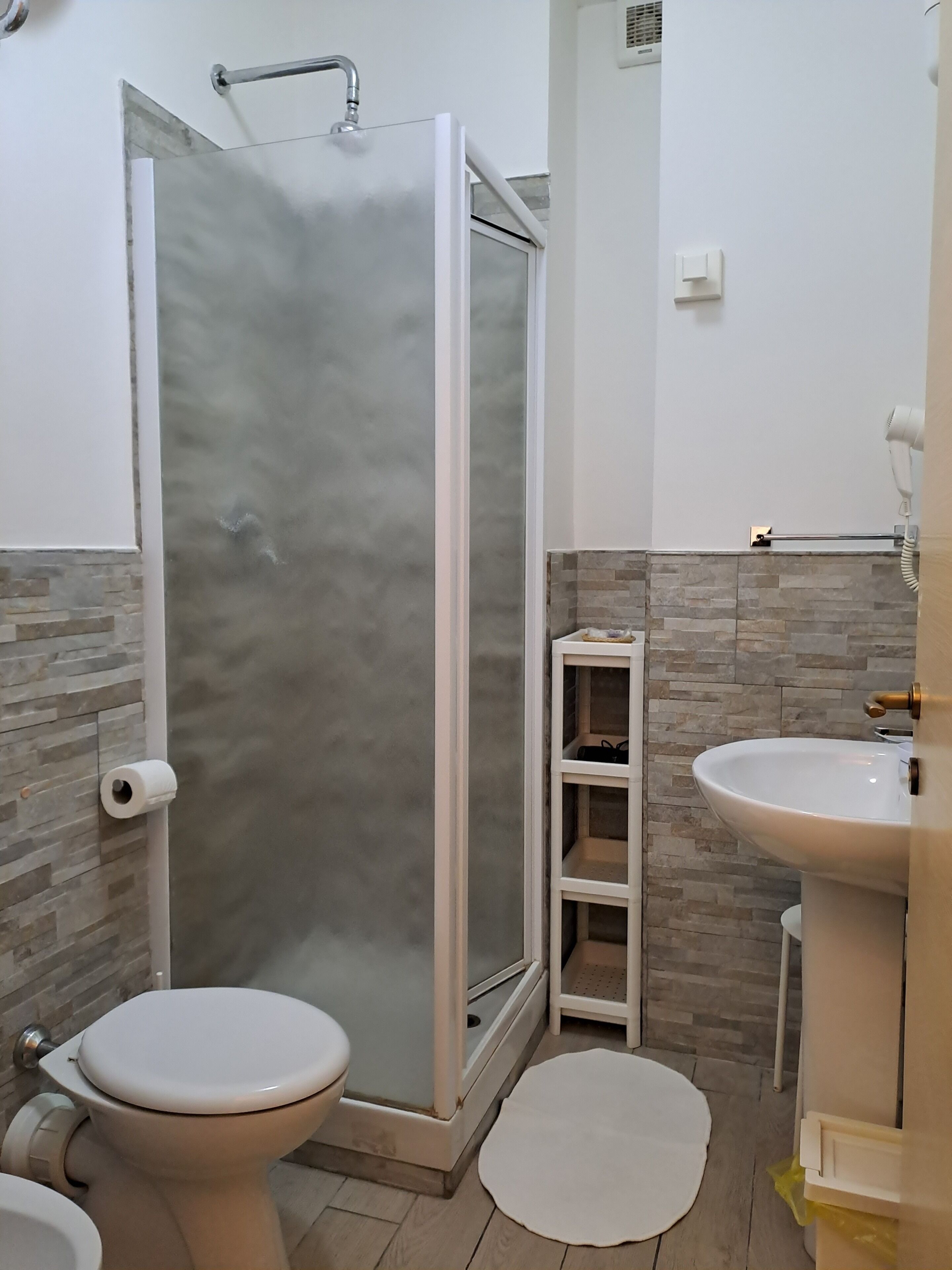 Ein Badezimmer mit Toilette, Waschbecken, Duschkabine und einer kleinen Ablagefläche.