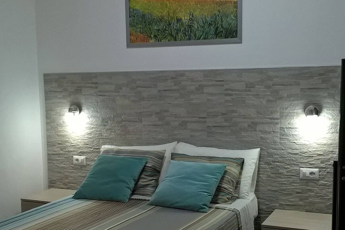 A bedroom with a bed, pillows, a nightstand, a dresser, and a painting on the wall.