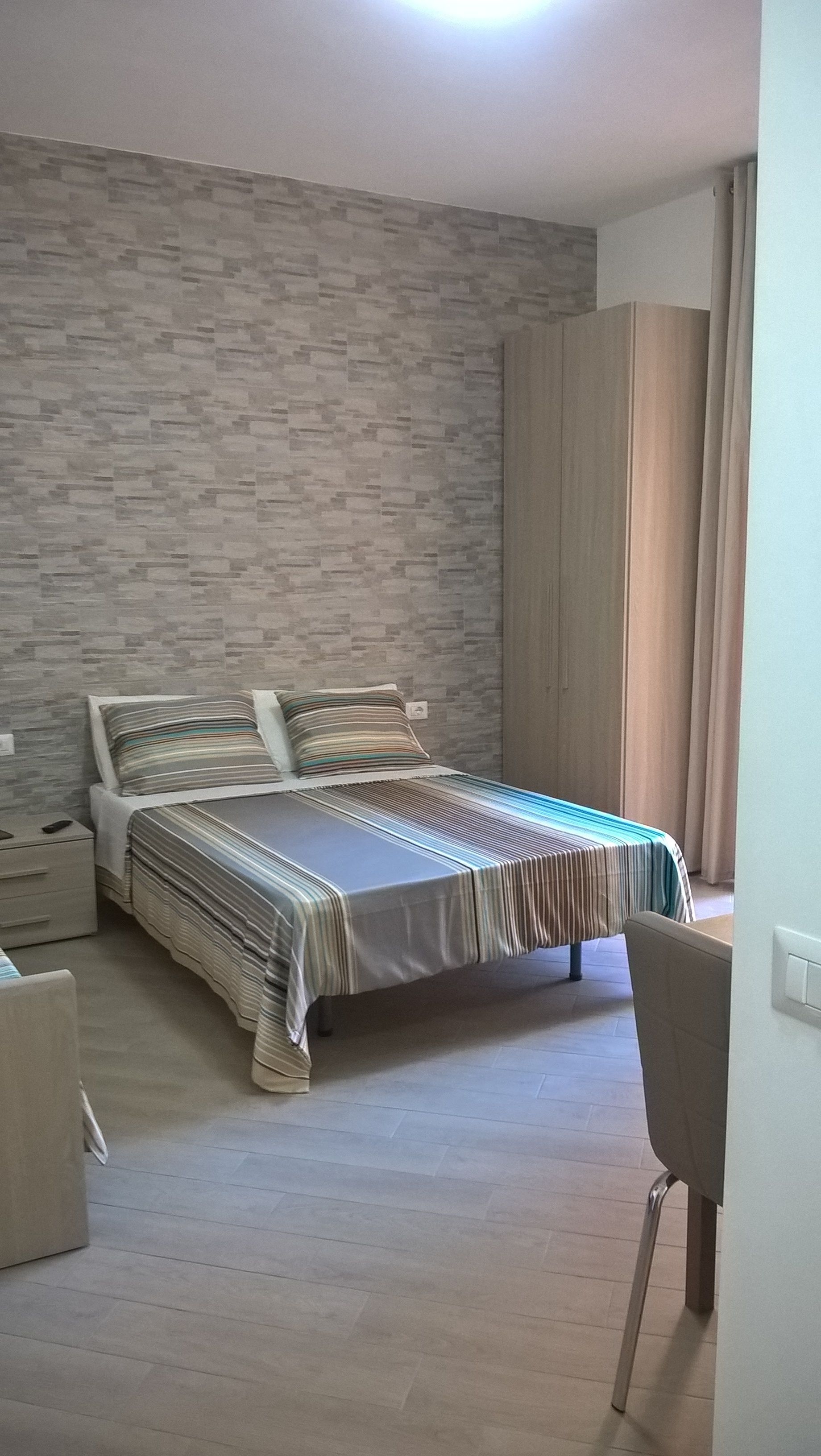 A bedroom with a bed, a nightstand, a chair, a wardrobe, and a curtain.