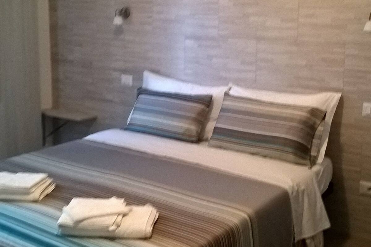 A modern bedroom with a large bed, a nightstand, and a wall-mounted light.