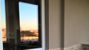 A window with a view of a sunset over a field, a stone wall, and a potted plant on a tiled floor. - Vacanza a Casa (Rome)