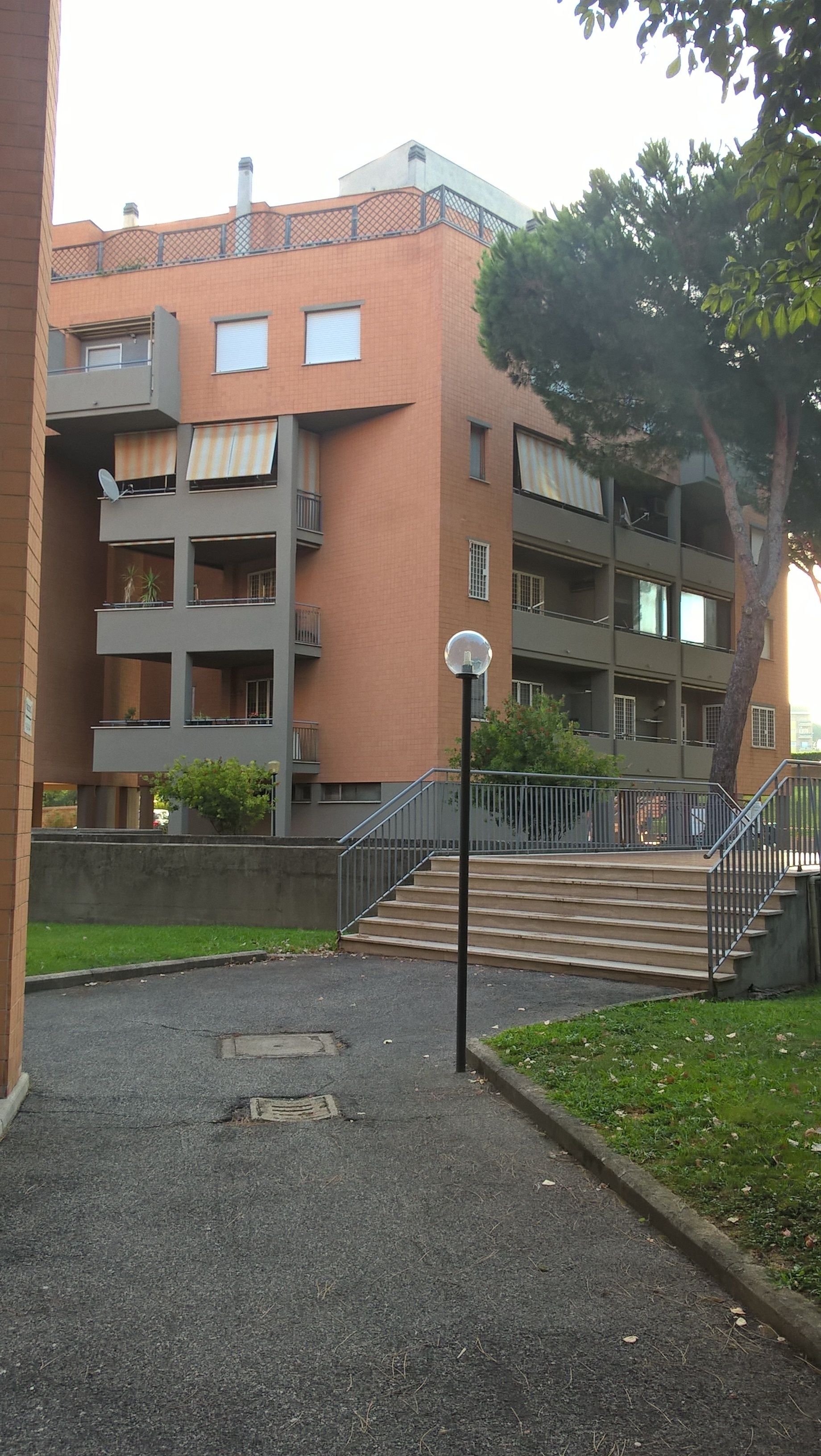 A multi-story residential building with balconies, a central staircase, and a street lamp.