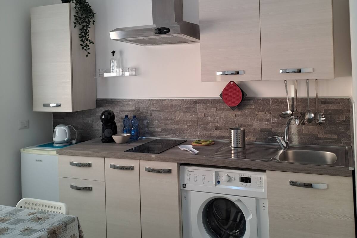 A compact kitchen with a built-in washing machine, a stainless steel sink, and a compact refrigerator.