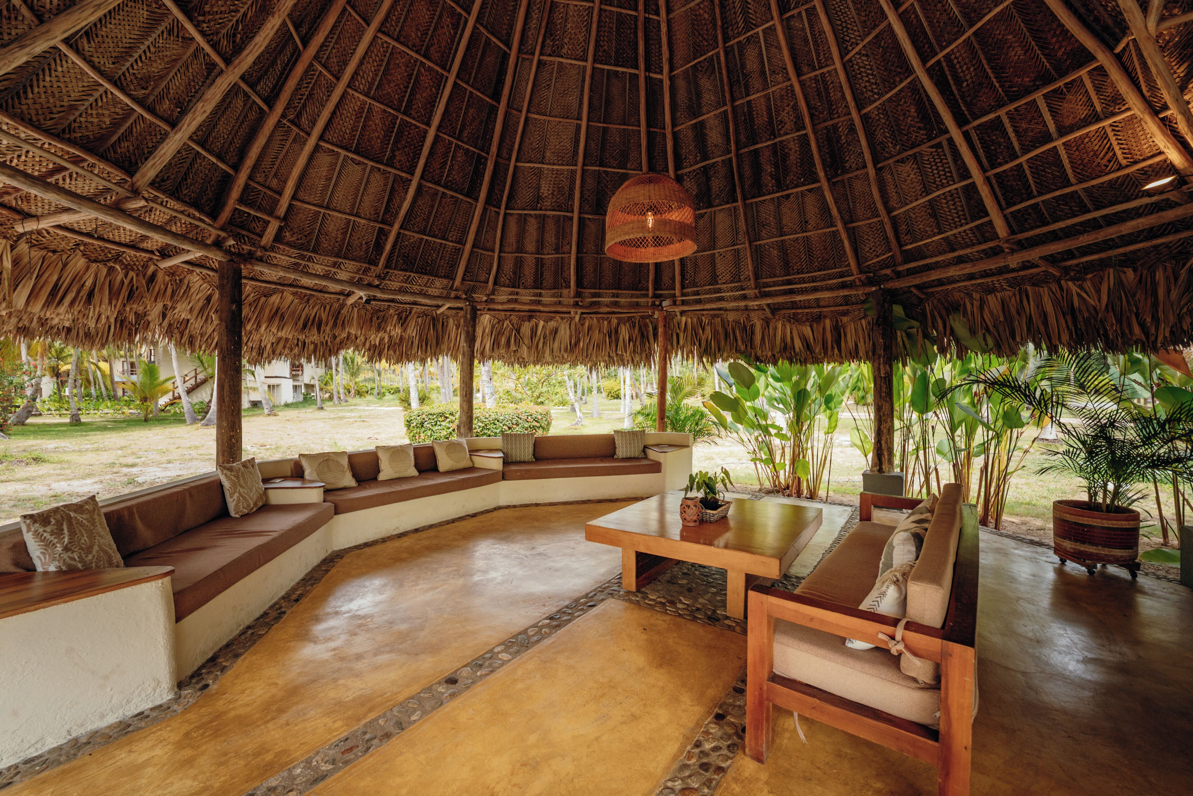 Un espacio lounge amplio con techo de paja, asientos acolchados y una mesa central.