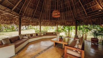 Un espacio lounge amplio con techo de paja, asientos acolchados y una mesa central.