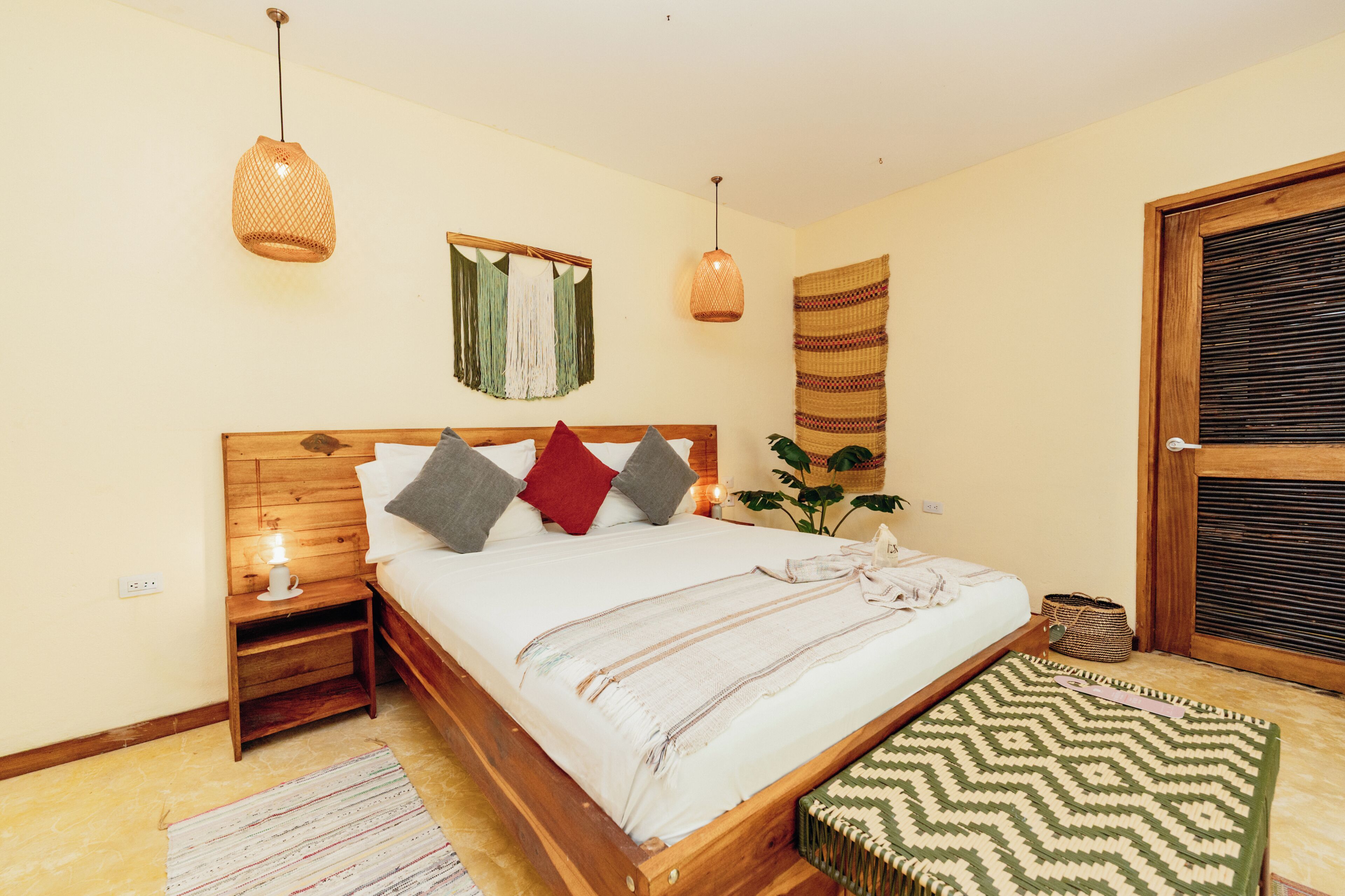 Un dormitorio con una cama de madera, lámparas de noche, un tapiz en la pared y un banco tejido.
