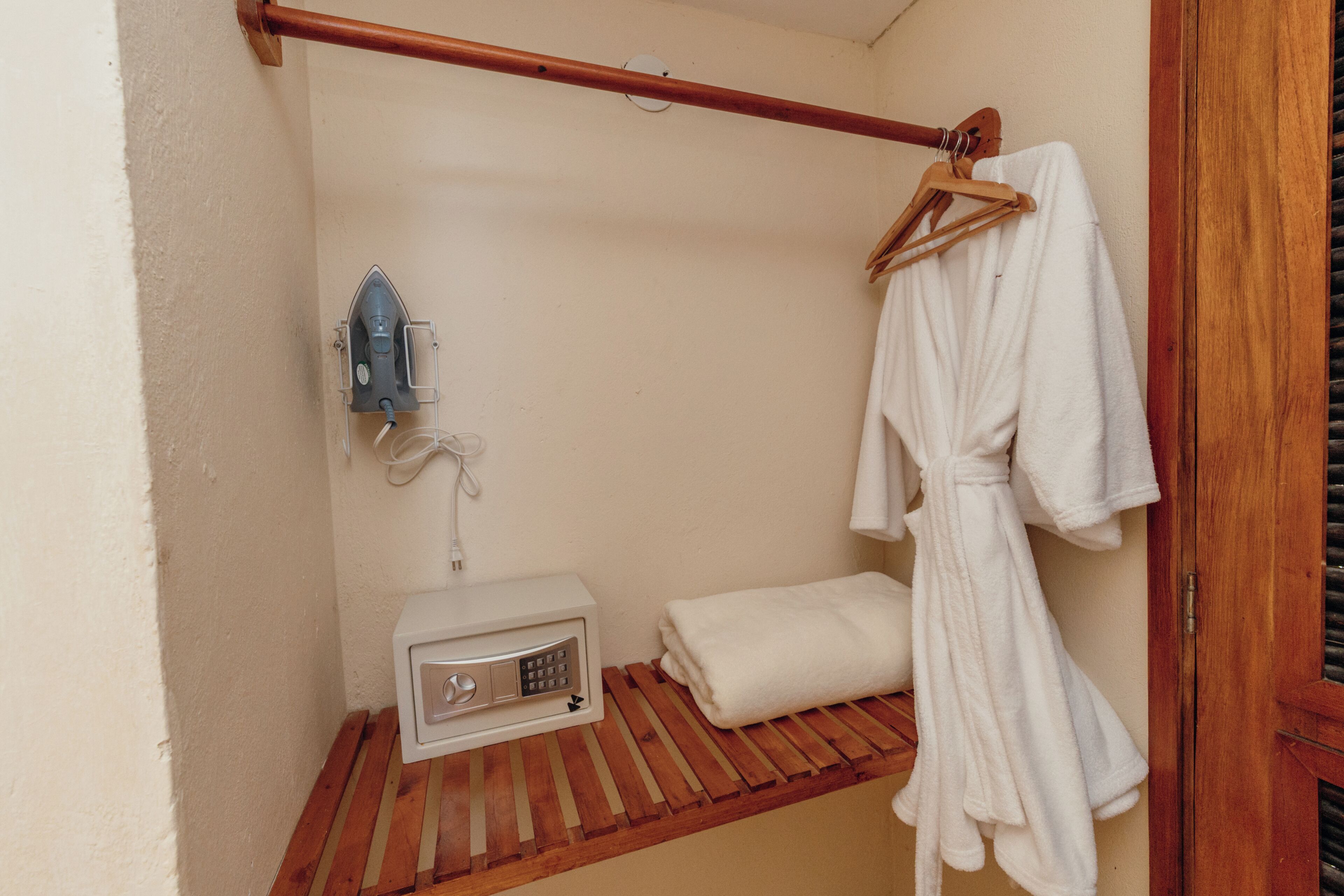 A small, enclosed bathroom with a wooden bench, a towel rack, and a wall-mounted heater.