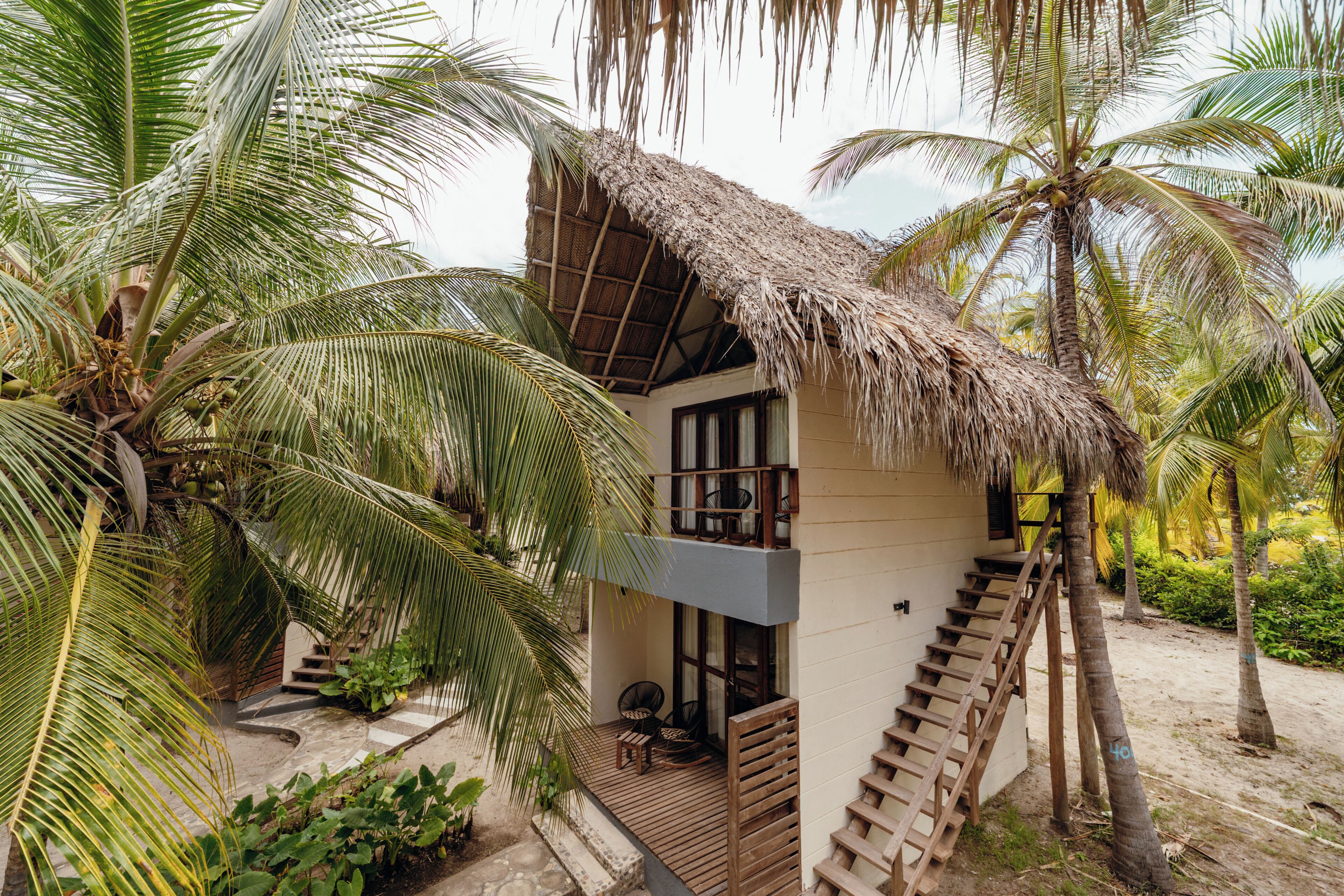 A two-story building with a thatched roof, surrounded by palm trees.