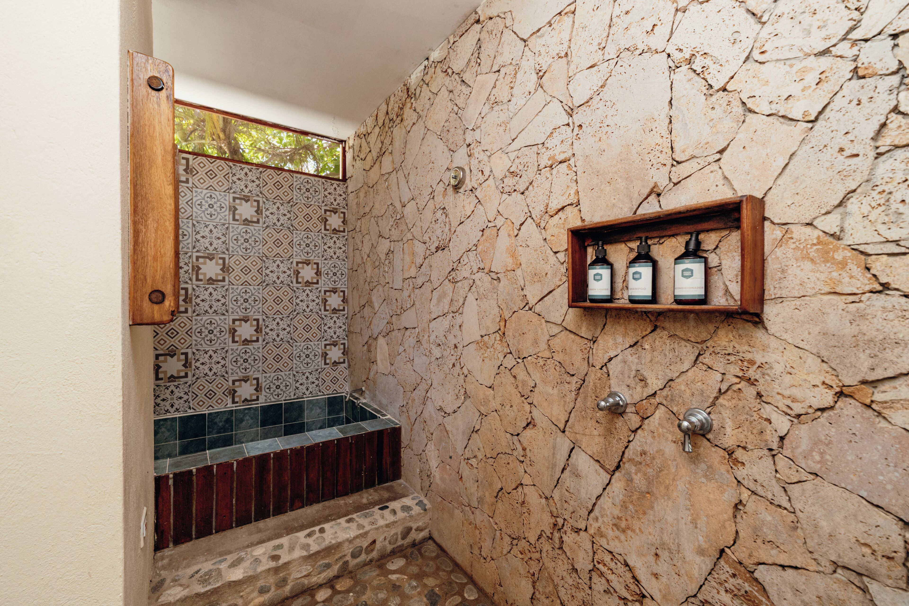 Un baño con pared de piedra, zona de ducha con azulejos y estante con artículos de aseo.