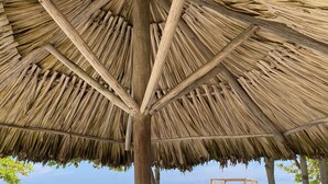 Una struttura parasole da spiaggia con due sedie di legno sottostante, con vista sulla spiaggia e sull'oceano.
