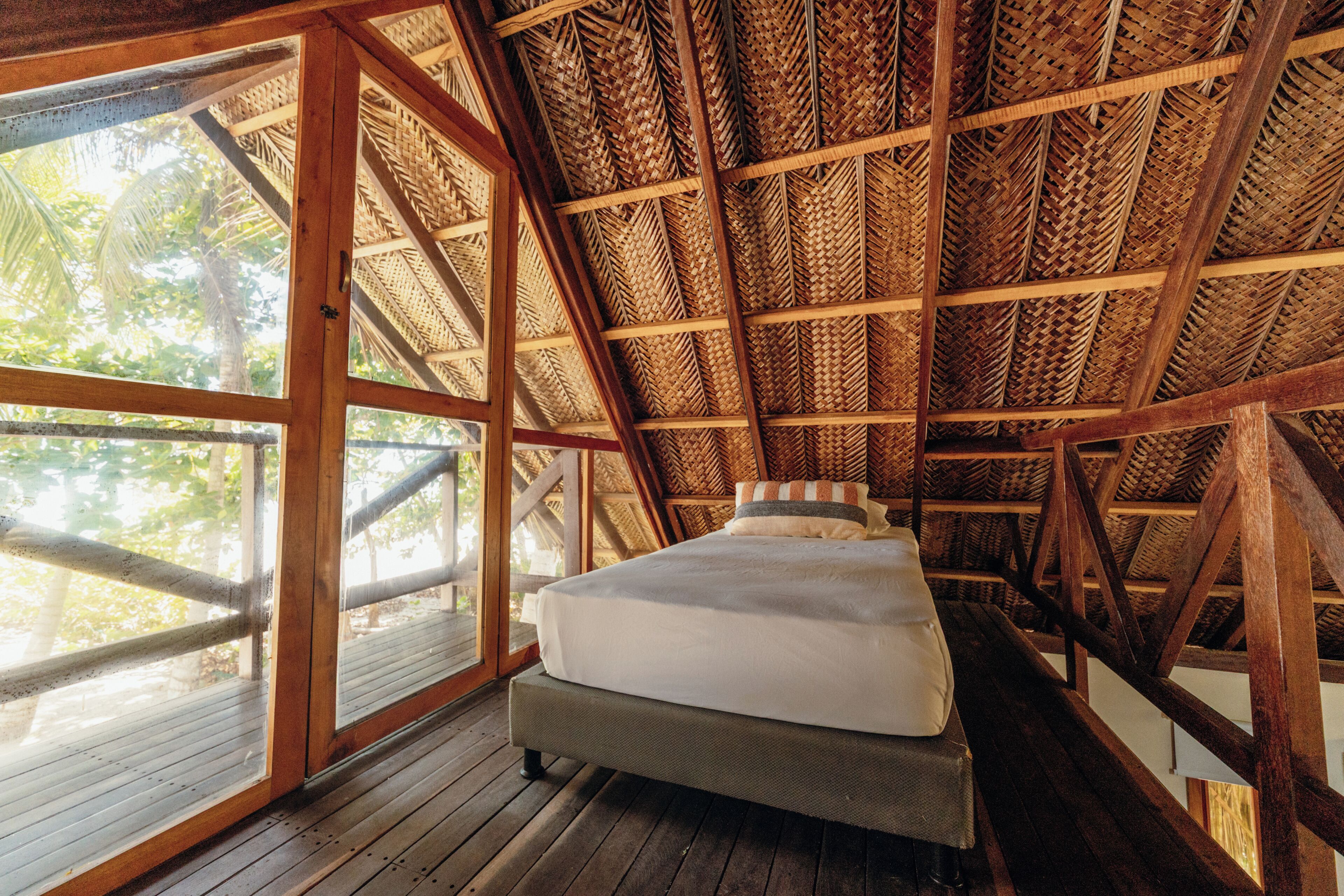A room with a bed, large windows, and a thatched roof.
