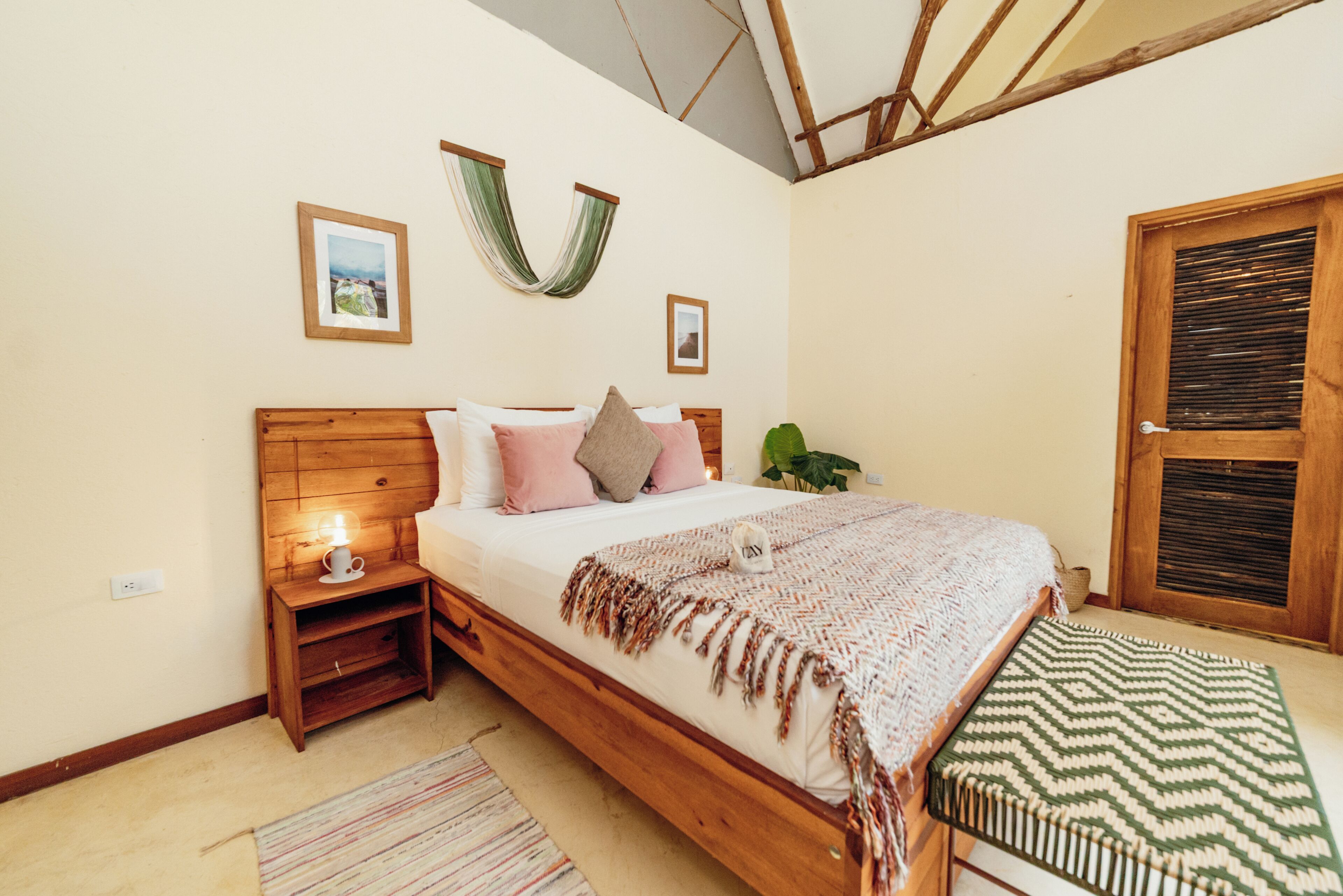 Un dormitorio con cama de madera, mesitas de noche, una planta colgante y una ventana con persianas.